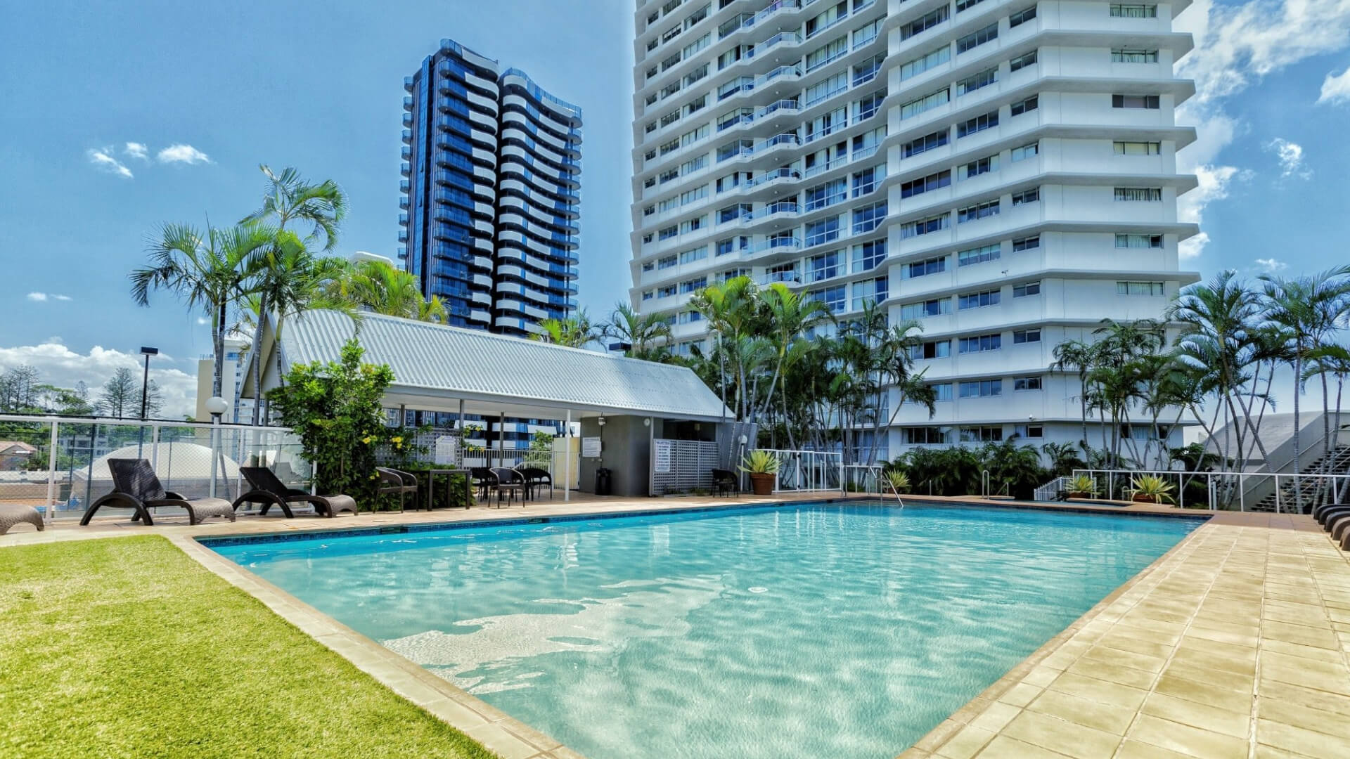 Outdoor swimming pool at ULTIQA Points North surrounded by sun loungers, palm trees, and high-rise buildings.