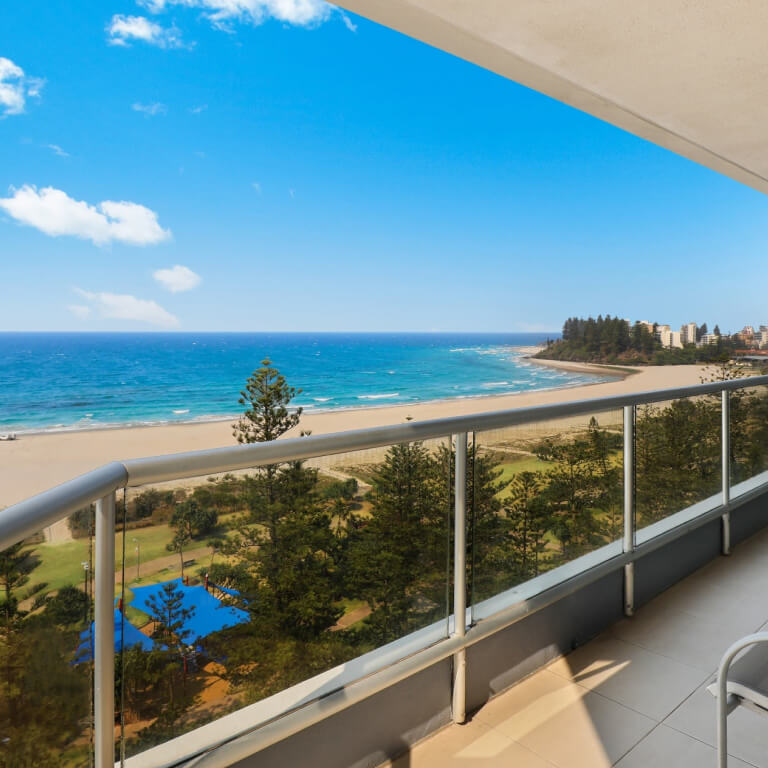 Ocean-view balcony at ULTIQA Points North Coolangatta with outdoor seating overlooking the beach, coastline, and sparkling turquoise water under a clear blue sky.
