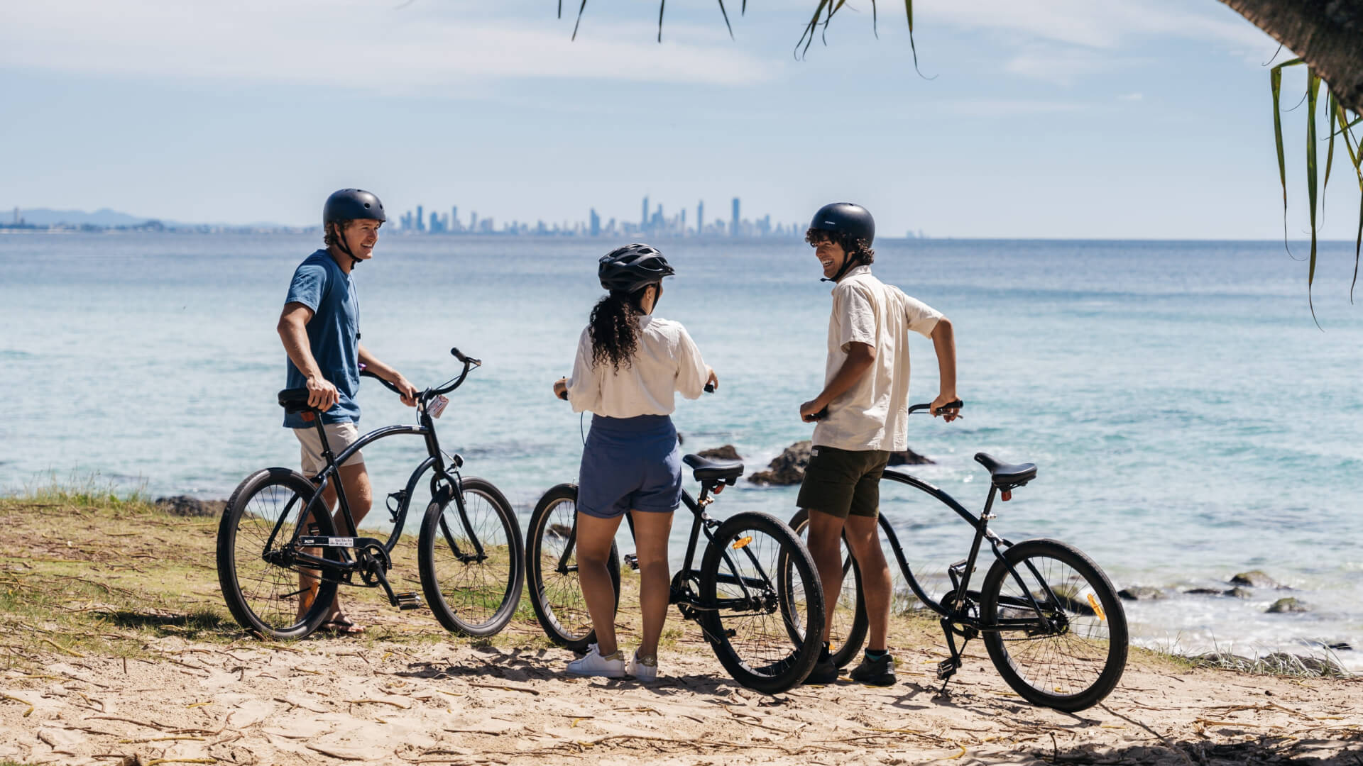 Group of friends with bicycles enjoying a coastal ride, overlooking the ocean with the Gold Coast skyline in the distance.