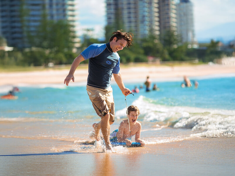 Father and son enjoying a fun day at the beach, playing in the shallow waves with boogie boards under the sun.