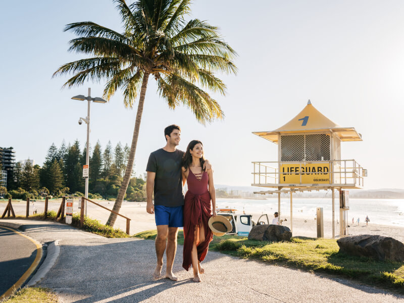 Couple enjoying a coastal stroll at Coolangatta Beach under palm trees.