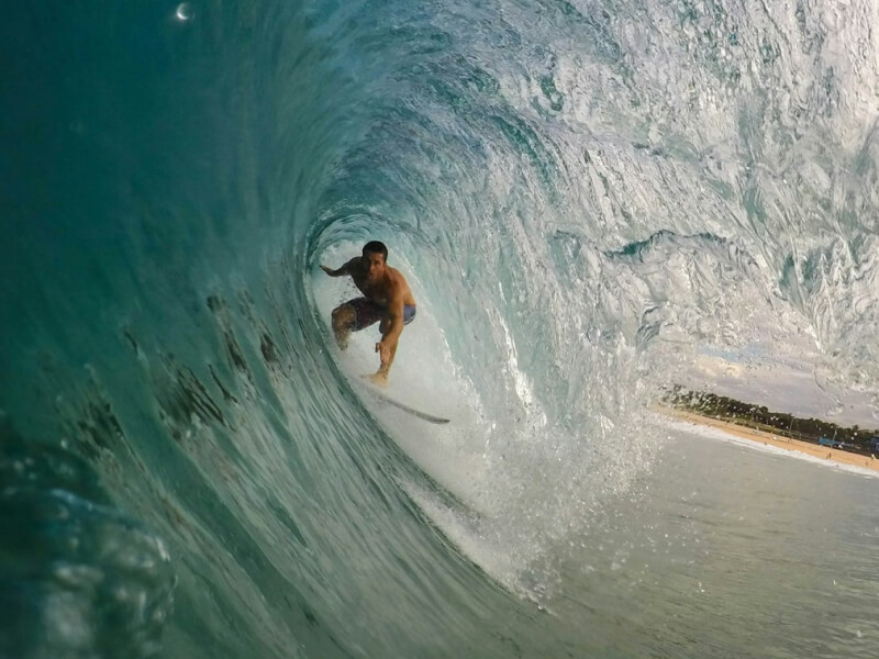 Surfer riding inside a powerful turquoise wave at Snapper Rocks on the Gold Coast, with the shoreline visible through the barrel.