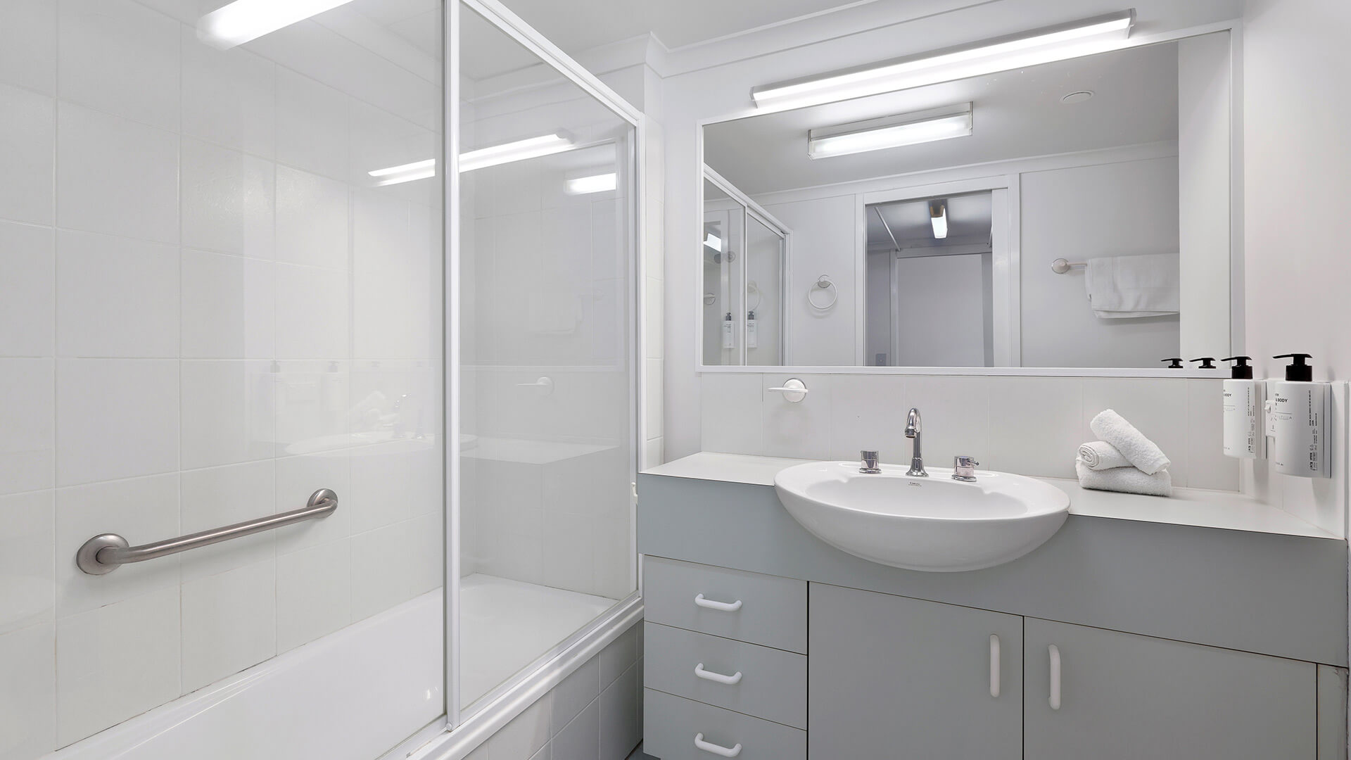 Bright bathroom with a shower-over-bath, large mirror, and ample vanity space.