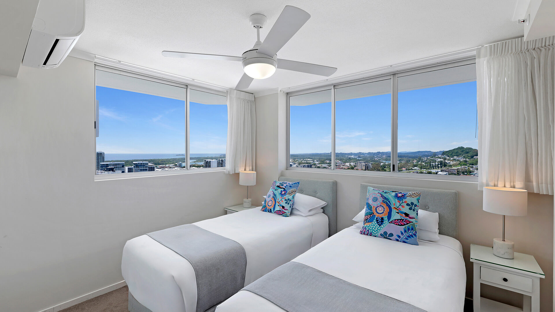 Twin bedroom in the Superior 3 Bedroom Ocean View Apartment featuring two single beds, soft coastal décor, and large windows with natural light.