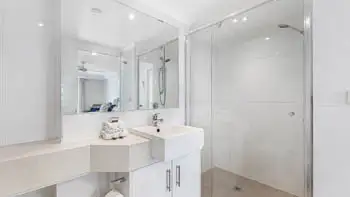 Bright modern bathroom with a large mirror, white vanity, glass-enclosed walk-in shower, and neatly folded towels on the counter.