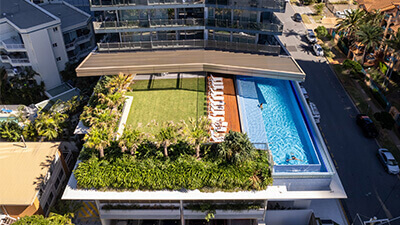 Aerial view of rooftop pool and sun deck at ULTIQA Signature at Broadbeach, featuring lounge chairs, greenery, and modern apartment balconies.
